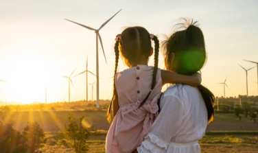 A young lady holding her child looking at the windmills during sunset.