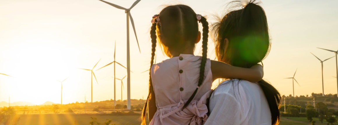 A young lady holding her child looking at the windmills during sunset.